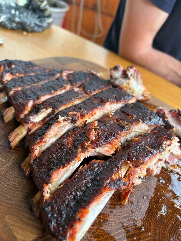 Рёбра с тёмной BBQ-корочкой, нарезанные на деревянной доске